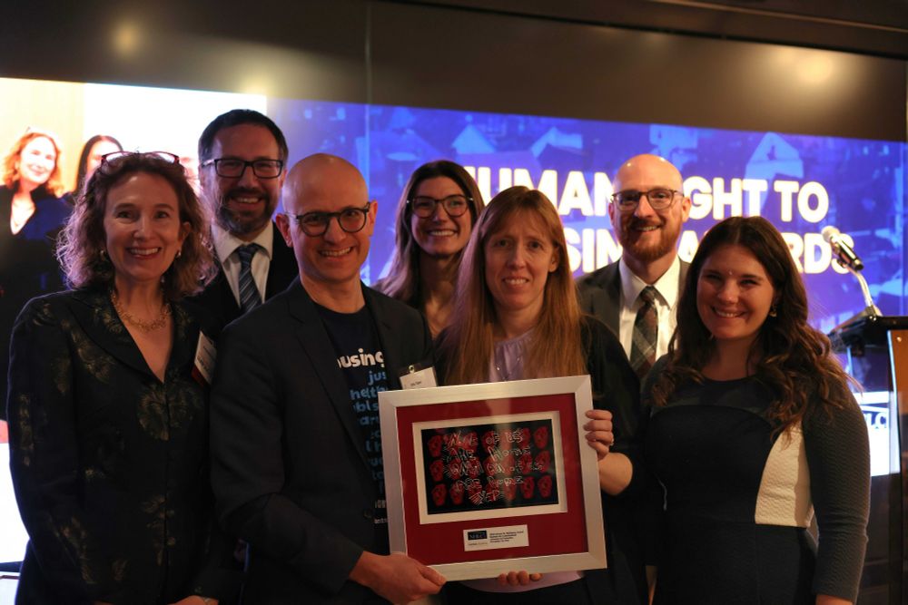 7 people gathered around a rectangular-framed award.