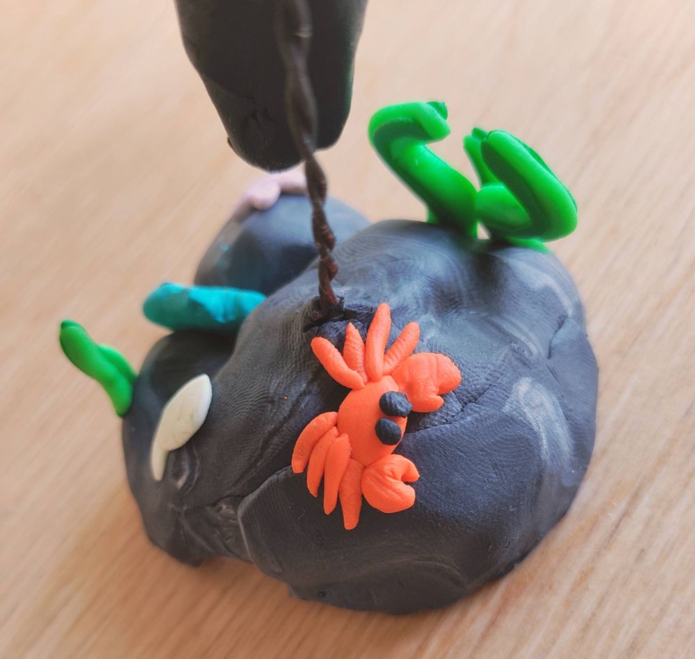 A closeup of the stand for the statue/figure/thingy (i dont know what to call it im so sorry ;w;) The stand is sea themed and has kelpy bits, a clamshell, a fish, a starfish and a silly crab :3