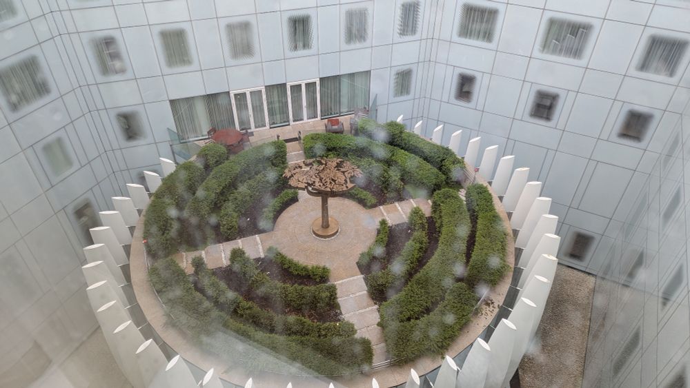 View of a round plaza with a white building and funky windows behind it
