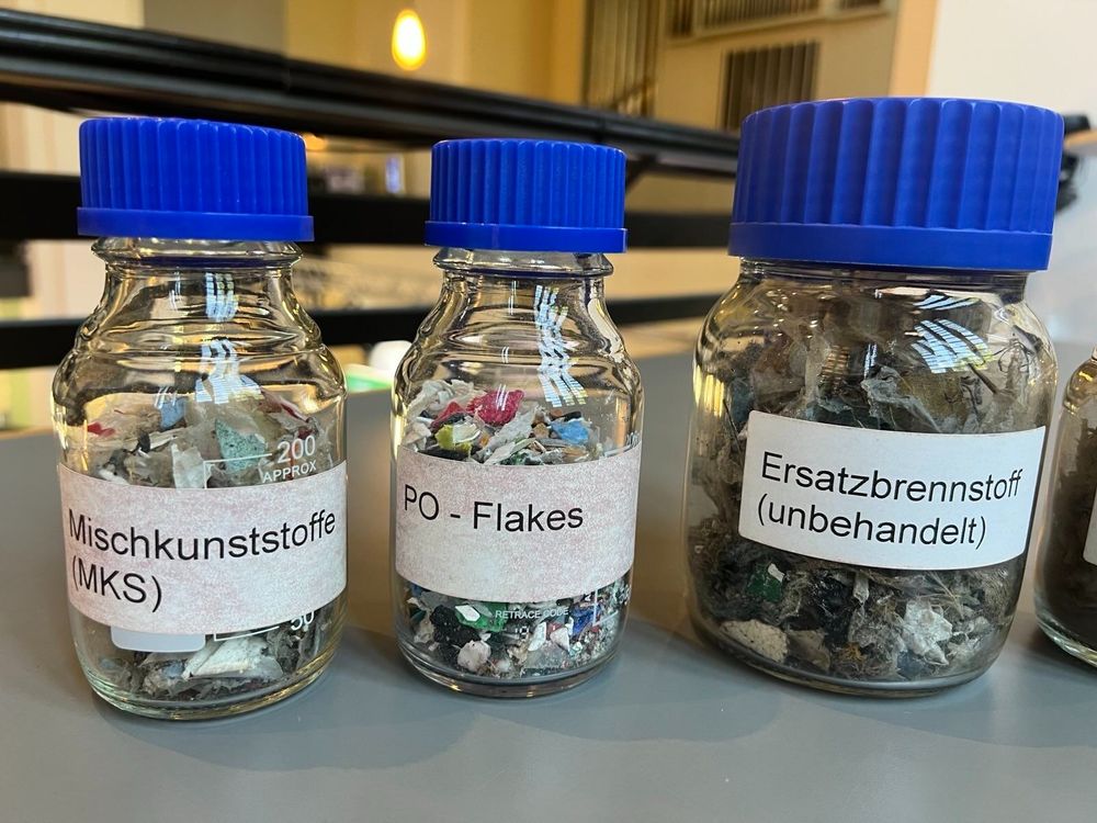 Drei kleine Fläschchen mit buntem Inhalt. Sie tragen Etiketten, die erklären, um welche Art von Kunststoff es sich handelt.