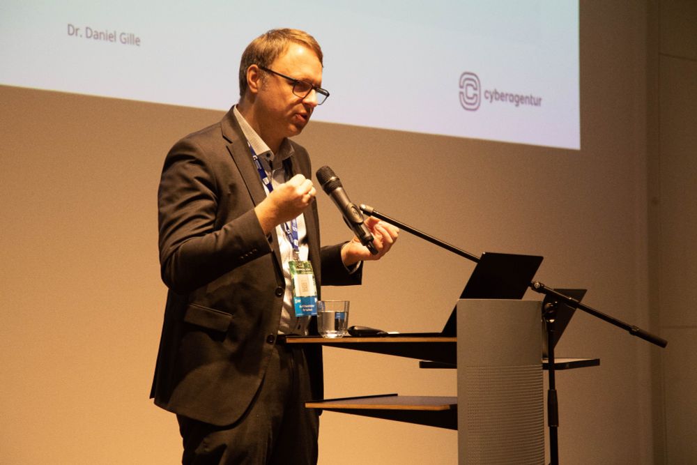 Das Bild zeigt Dr. Daniel Gille, Referatsleiter Künstliche Intelligenz bei der Agentur für Innovation in der Cybersicherheit GmbH (Cyberagentur) bei einem Vortrag auf dem IT-Sicherheitstag Dresden 2025.  