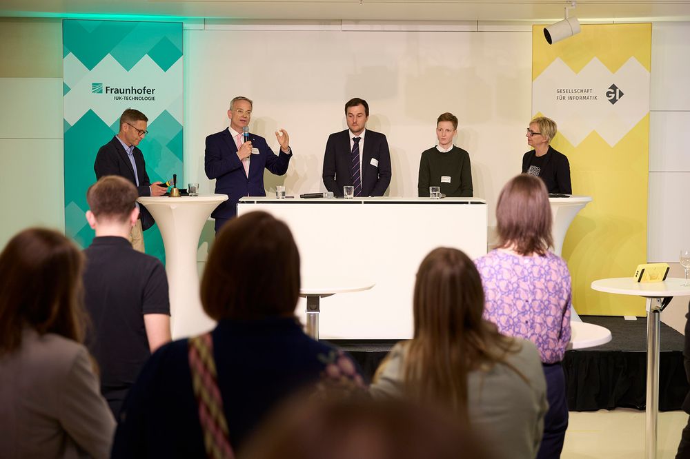 MdB Markus Reichel spricht, mit ihm auf der Bühne Boris Otto vom Fraunhofer IUK, MdB Johannes Schätzl, MdB Rebecca Lenhard und GI-Präsidentin Christine Regitz, sie stehen zwischen Bannern für Fraunhofer IUK und GI