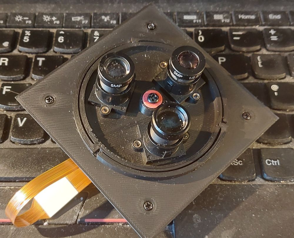 A 3d printed turret mechanism for a camera, with three M12 lenses on a circular platter. You rotate the platter to select the one you want.