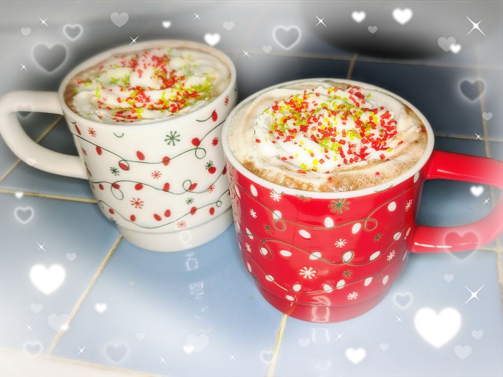 a photo of two white and red christmas mugs full of hot chocolate and whipped cream with red and green sprinkles.