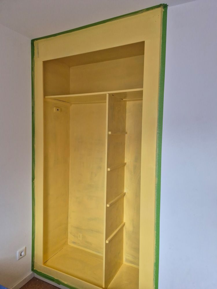 Eine Schranknische, die in hellem Gelb lackiert wurde. Um die Nische herum ist grünes Abklebeband geklebt. 