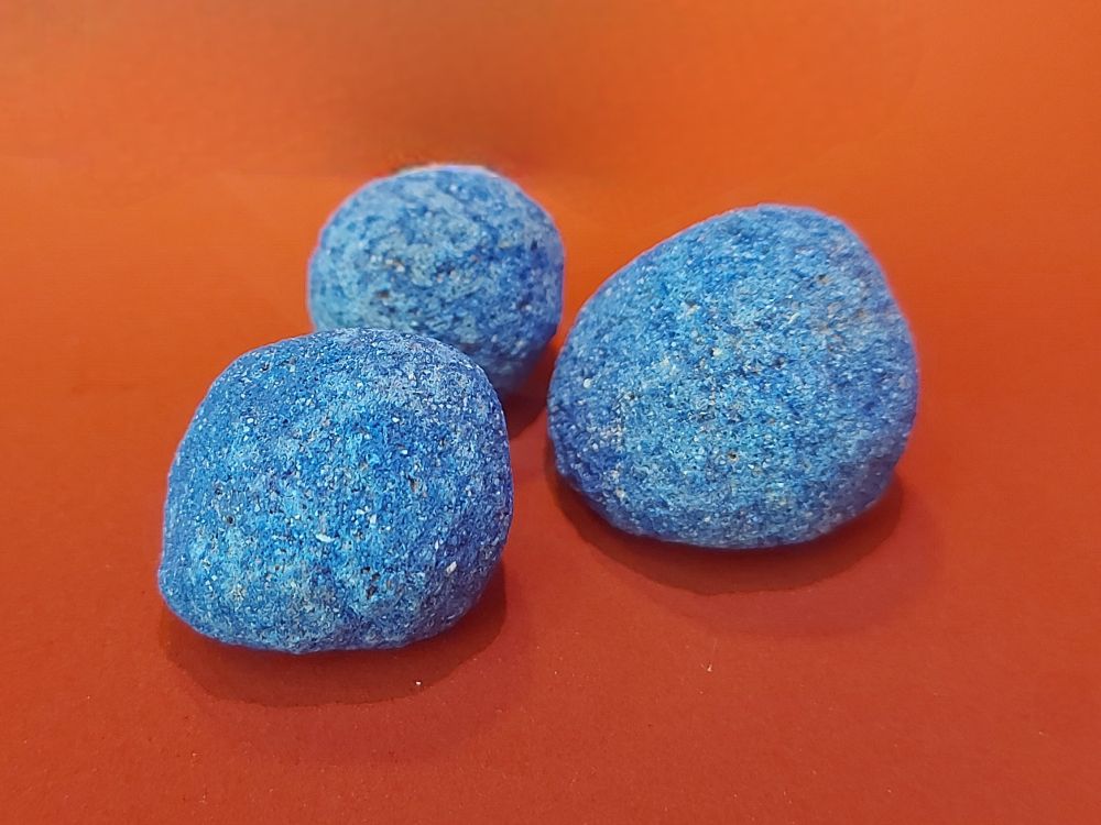 Three textured balls of bright blue pigment rest on a solid red surface, creating a vivid color contrast.