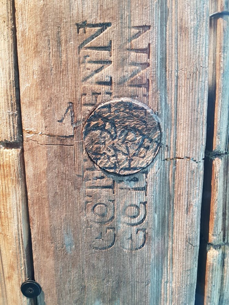 This is a close-up view of the wooden barrel, showing an engraved stamp on the wooden surface. The letters are partially visible and slightly faded due to age.