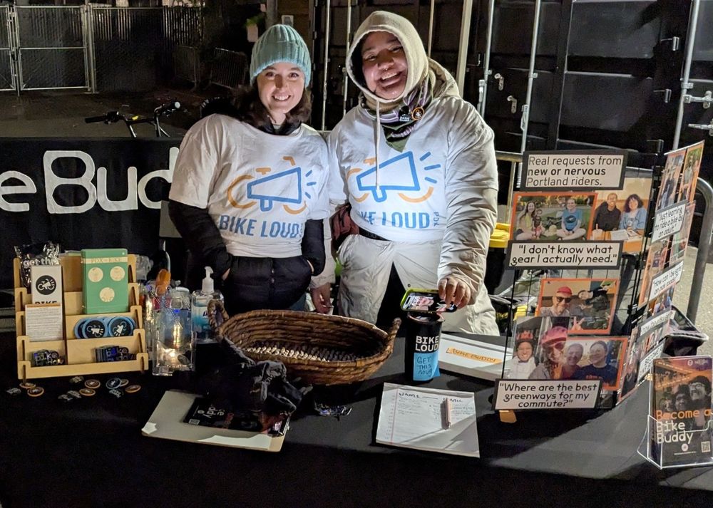 Kiziah & Nikki Margarita welcome people picking up their bikes at GoByBike bike valet to sign up as Bike Buddy mentors. They have some small posters that explain the program. 