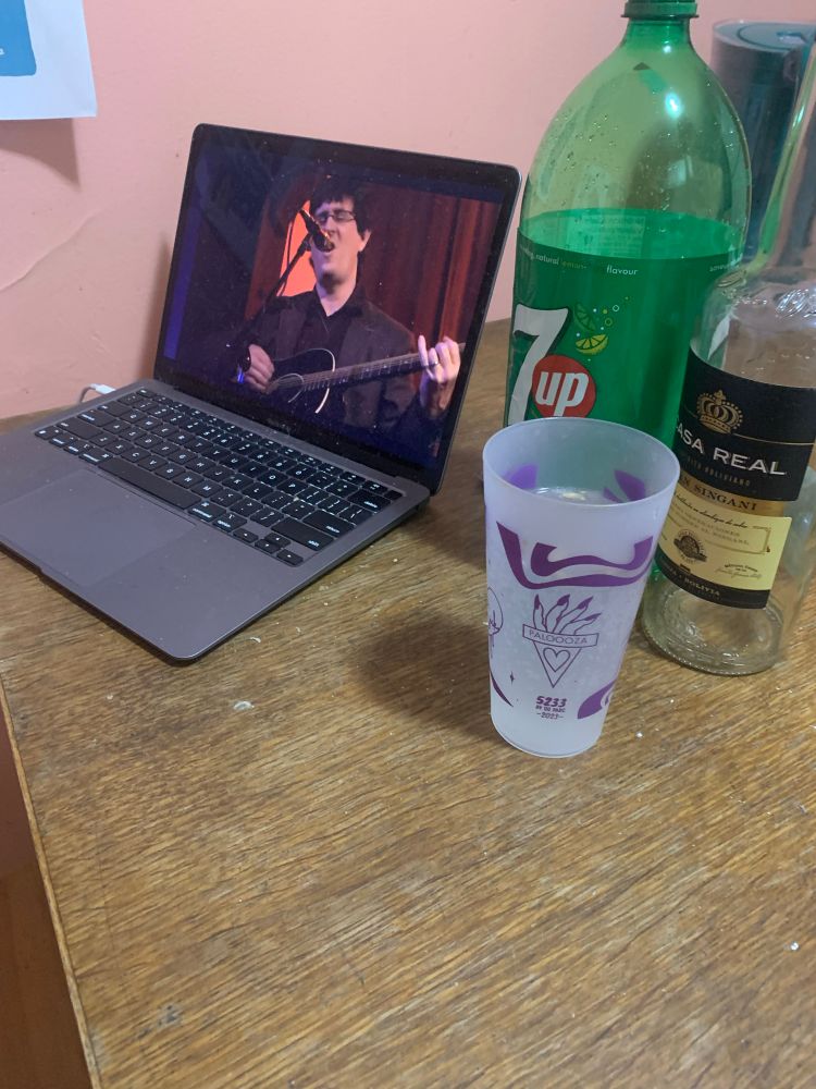 Laptop with a video of the mountain goats playing live at the Swedish American hall. There is a glass with a chuflay cocktail besides a bottle of sprite and Singani (2/4 of said cocktail)