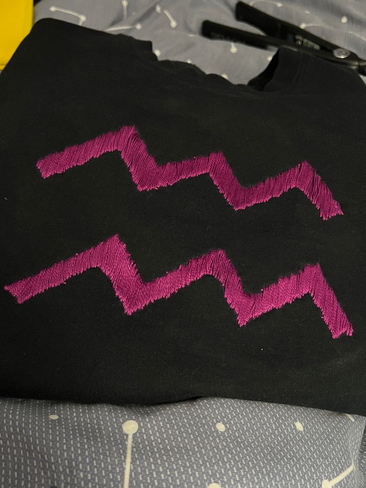 photo of the homestuck aquarius symbol hand embroidered on a black sweater