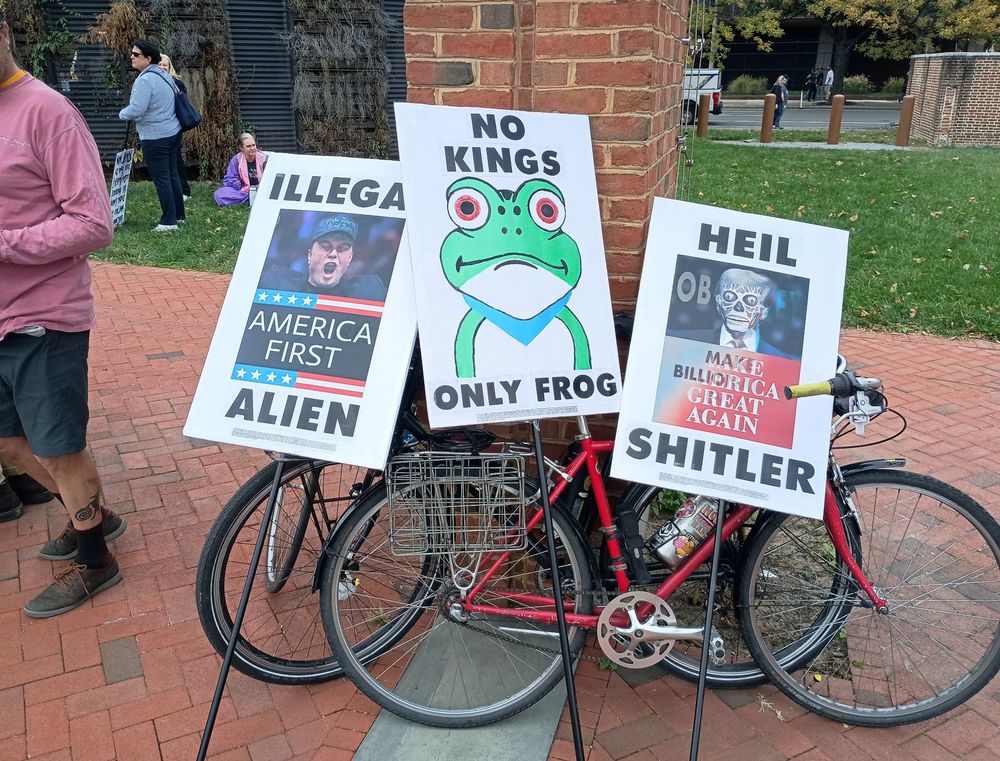 Various signs from no kings. One says "no kings only frog" one says "heil Shitler" with a they live style 3d animation of Trump. The other says "illegal alien" with a they live style 3d animation of Elon Musk. 