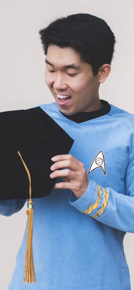 Photo of Dr. Mike Wong wearing a science blue tunic and holding a doctoral tam.