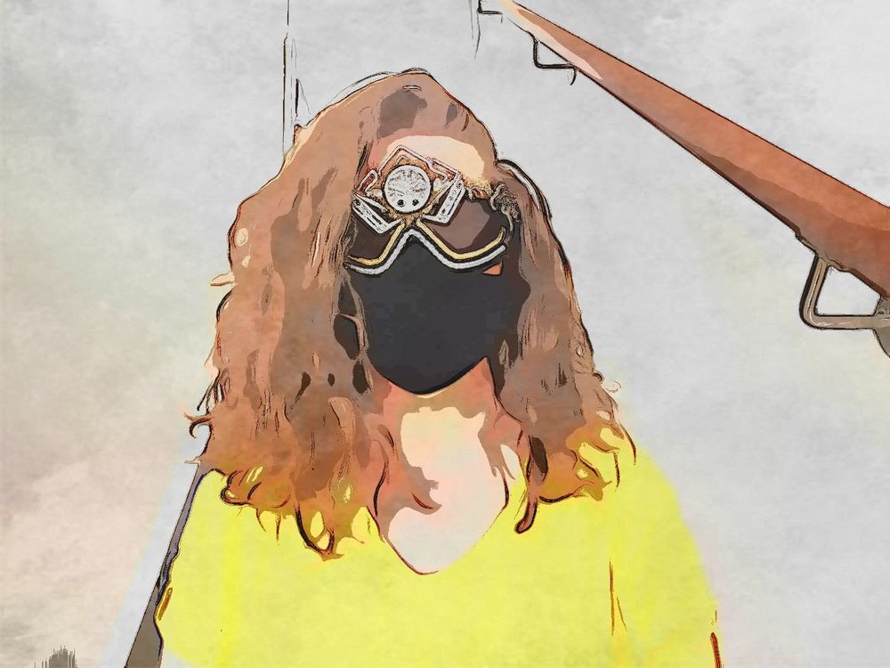B sits in a staircase. She wears a sunshine yellow g shirt, a black velvet face mask and ornately decorated ski-style goggles. Her hair is messy, golden, curly. The photo is stylised.