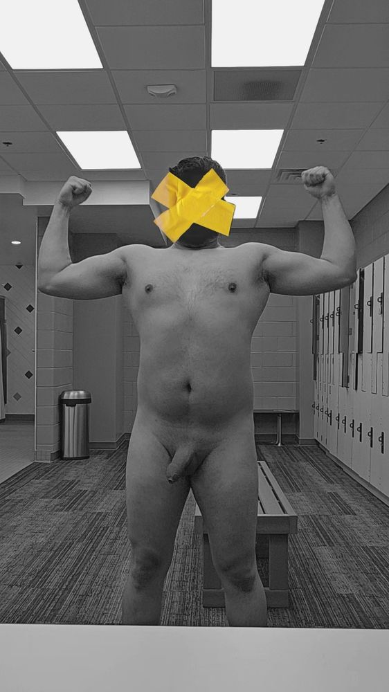 Black and white picture of naked man flexing in a locker room. The perspective is from inside an open locker. Yellow tape hides his face