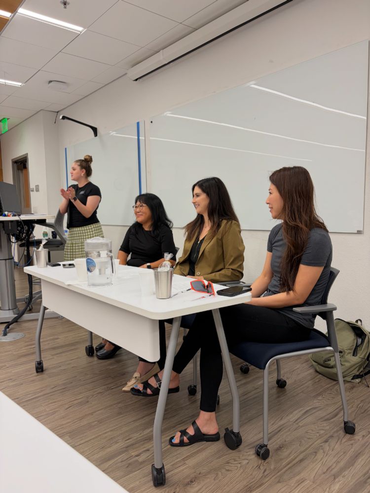 Three GPS alumni smiling while seated at a table inside a classroom.