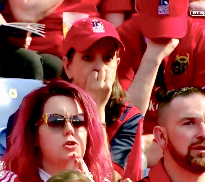 Hilary nervously looks on from the crowd of Munster supporters, her hand is covering her mouth like she is biting her nails. The guy behind her has his head down and his 
hand covering his face. 