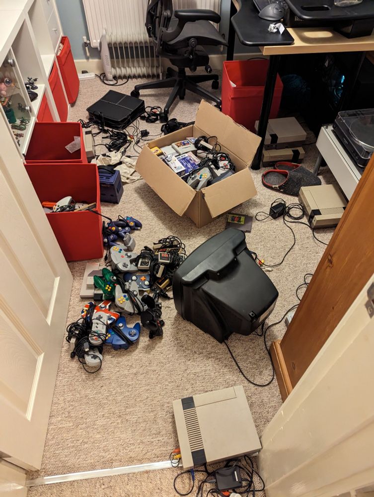 My office floor covered in retro consoles, wires, cartridges, and controllers. There are four Nintendo Entertainment System consoles amongst the debris.