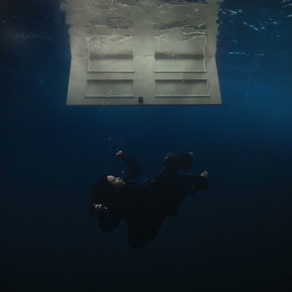 Imagen de la portada del álbum "HIT ME HARD AND SOFT" (2024) de Billie Eilish, en la que se ve a Billie sumergirse en el agua tras abrir una puerta, en una imagen surrealista.