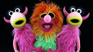 3 muppets, from the mahna mahna song performed in 1969. Main muppet is a male singer with bright orange hair, yellow sunglasses, pink nose and green body fur. the 2 backup singer muppets look like pink space creatures with horns and body fur, yellow lips and big eyes with long eyelashes