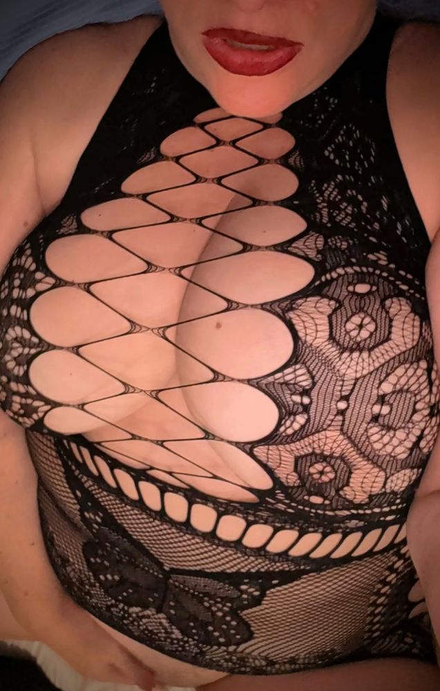 Polly is wearing a black lace and fishnet skin tight dress with an entirely open bust with wide net across holding it together somehow. Her red lippy is partially worn off on her parted lips and her hand is in the distance on the bottom, playing with her bare pussy. This, my dears, is what domming from the bottom looks like.