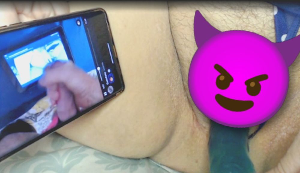 Close-up of Poly's pussy (obscured by a devil emoji) with blue polka dot panties pulled to the side and a turquoise dildo slid into her. Her phone is by her thigh and has Cumfy's cum tribute video on it. He is jerking off in Poly's favourite of his panties and is looking at Poly on his screen. It's a cumception!