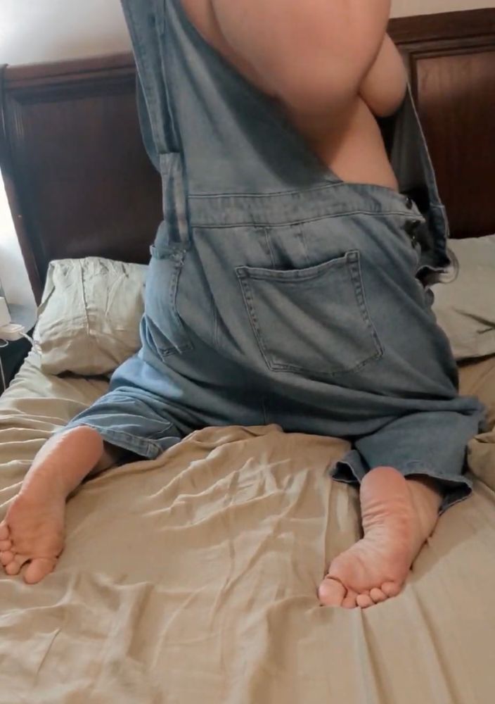Holly is kneeling on the bed at the pillows faced away from the camera wearing overalls and no shirt. Her feet pointed out towards the viewer and her shoulder and elbow are back revealing a bit of side boob. It's not twerking to Alana Miles, but it's not too bad.