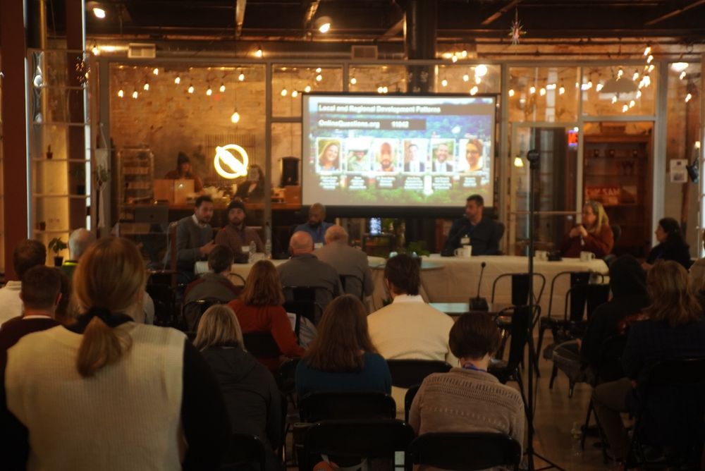 A well attended panel meeting about local urban planning organizing hosted in the middle of a small mall space with a lot of glass windows.