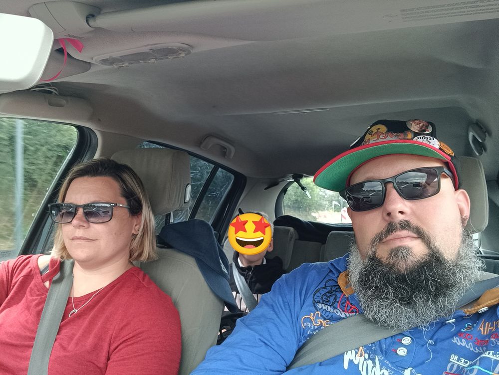 Photo à l'intérieur d'une voiture.
Ma compagne qui conduit, moi qui prend la photo et l'enfant à l'arrière avec le visage caché par un smiley. 