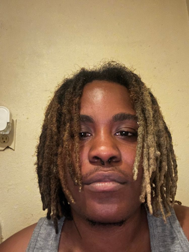 moe with locs down that are half green & brown with gray tank top on. 