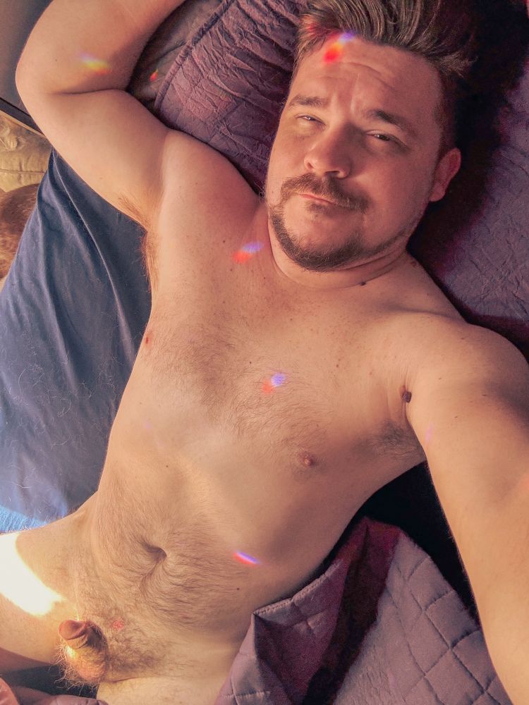 Laying naked in bed with little rainbows all over me 
