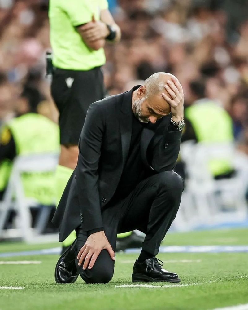 Pep Guardiola holding his bald-head in anguish, with one arm on his knee to the ground.