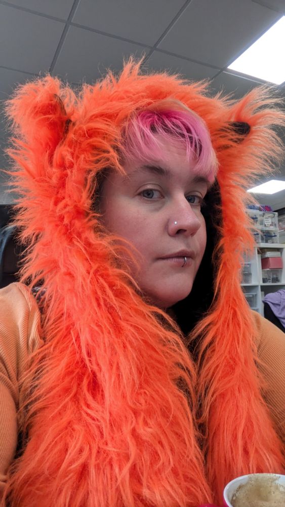 Tired looking person in a very fluffy orange hat with ears