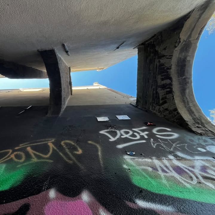 Foto, omhoog genomen in een nauwe straat tussen twee gebouwen, er zijn stenen bogen zichtbaar. Op de muur is graffiti gespoten.