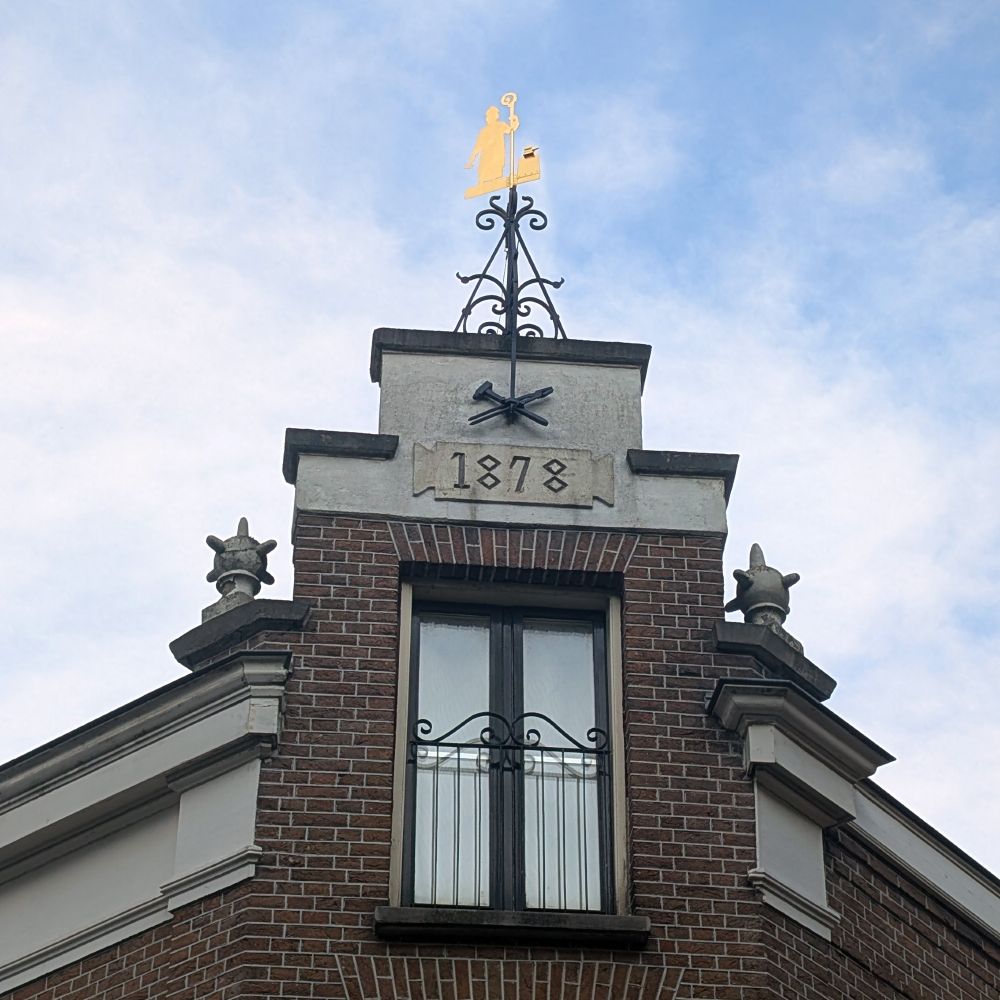 Getrapte gevel met jaartal 1878 en windwijzer van een heilige.