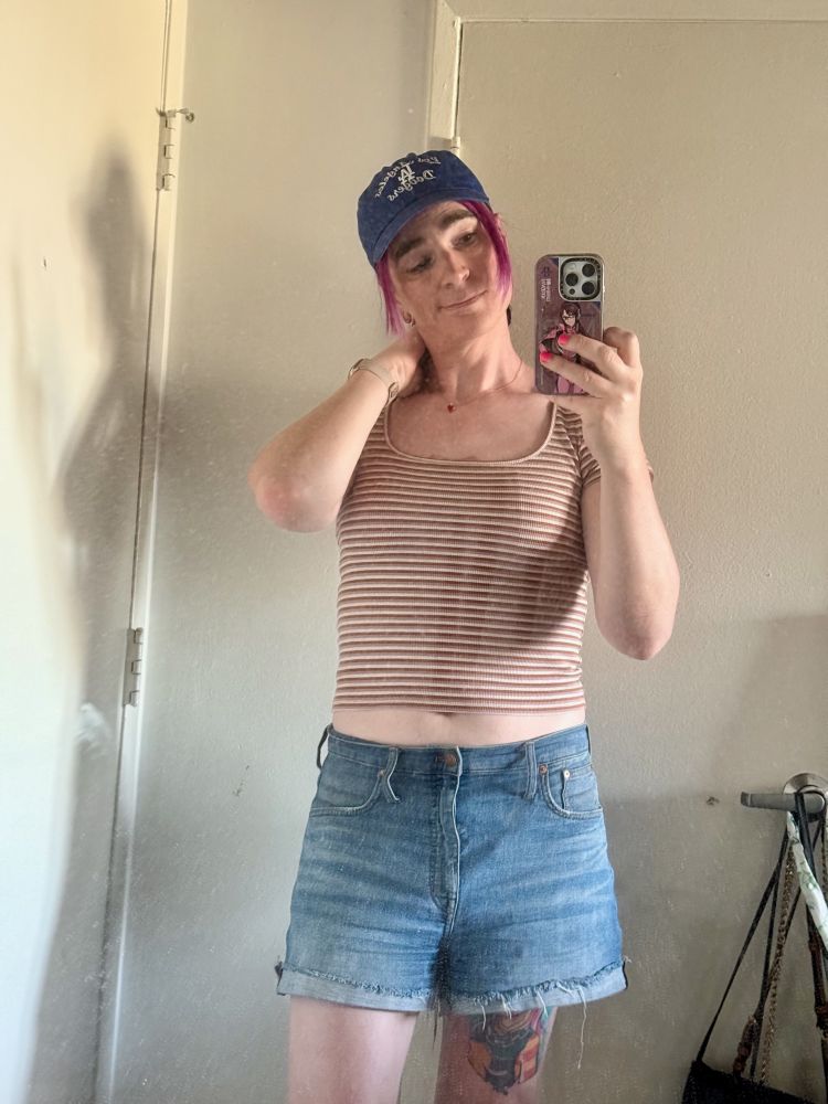 becs in denim shorts and a pink striped tee, wearing a dodgers baseball cap, and smiling at the camera