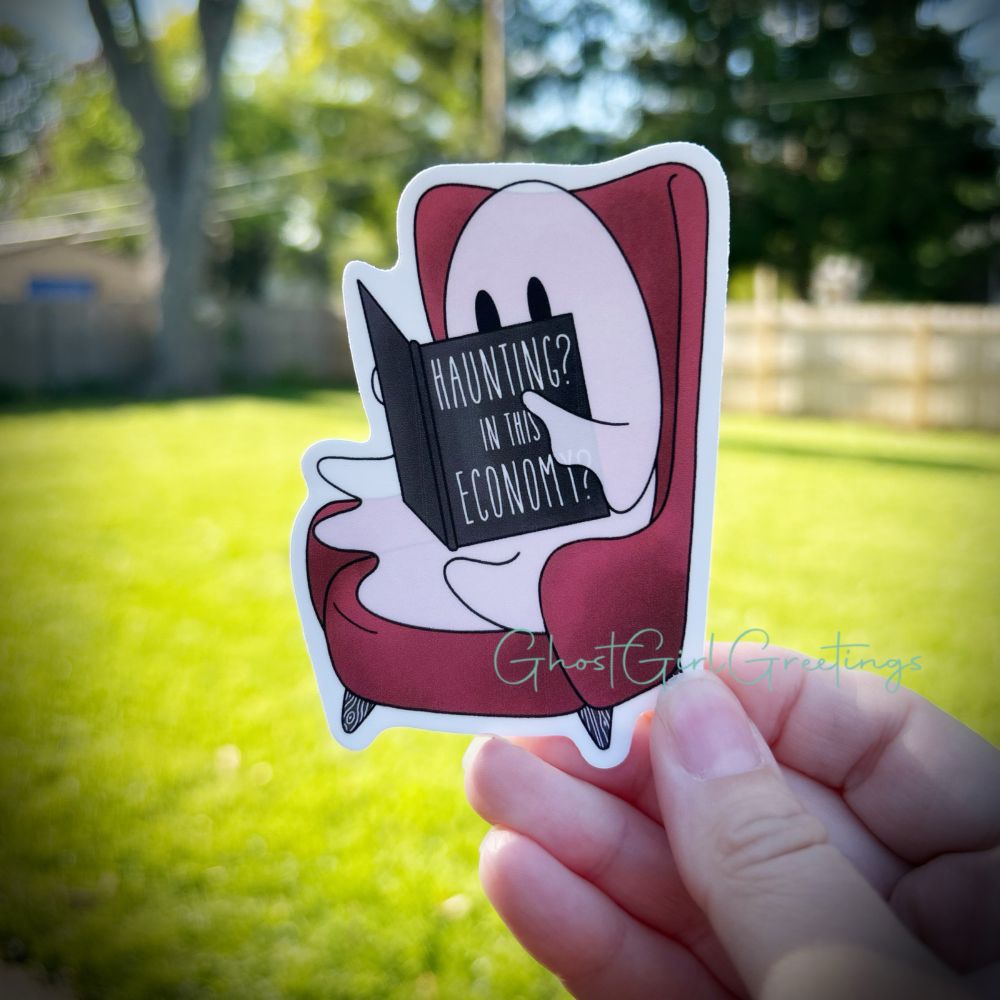Sticker of a Ghost reading a book that with cover “Haunting? In this economy” 