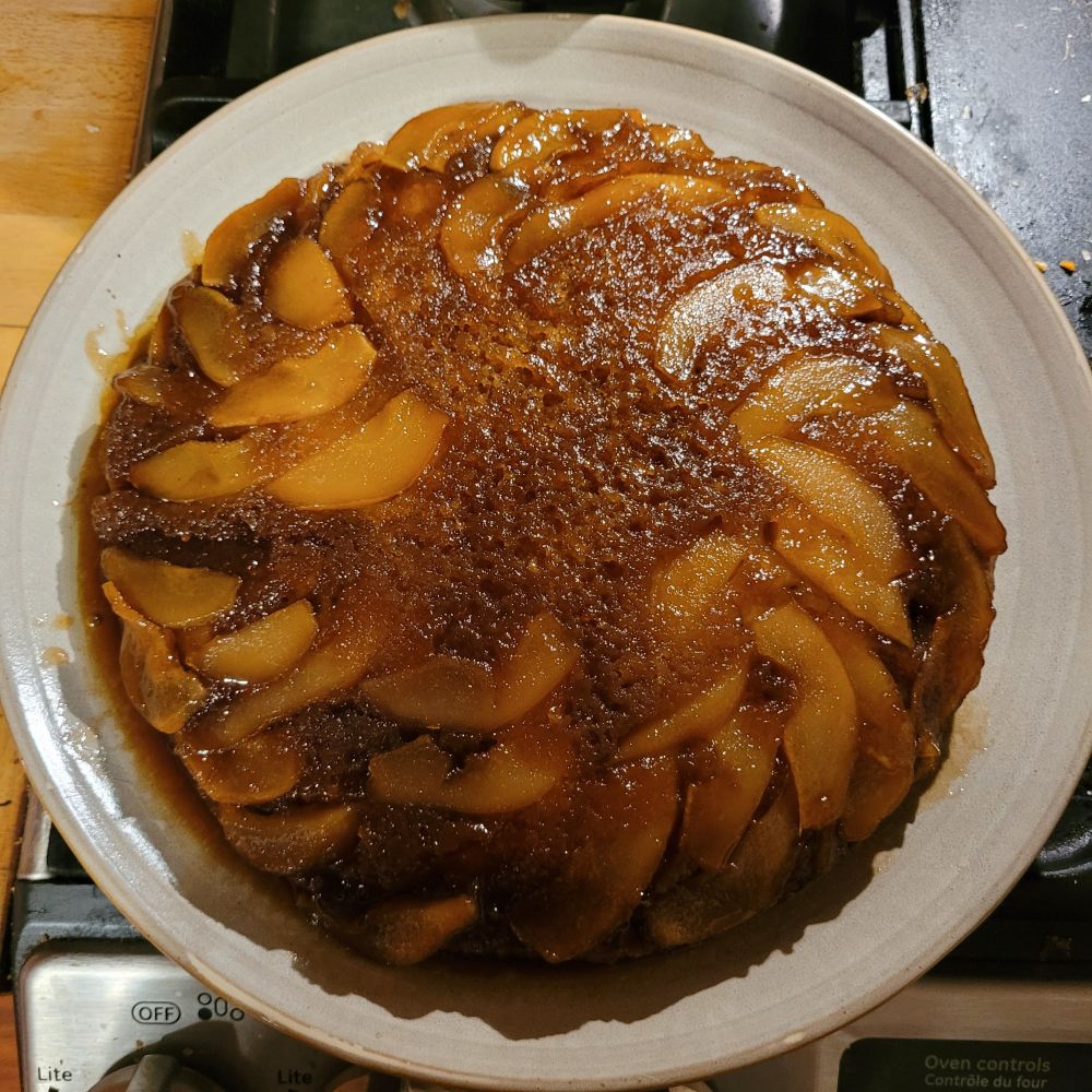 A bird's eye view of an upside down pear cake. The cake is sticky with treacle and the pear slices are fanning from the centre. 