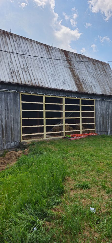 Old gray barn with gray metal roof and mounted new sliding doors frames. The door frames are constructed with 25 sections that are still uncovered. We are waiting on the board and batt pieces to cover the door. 