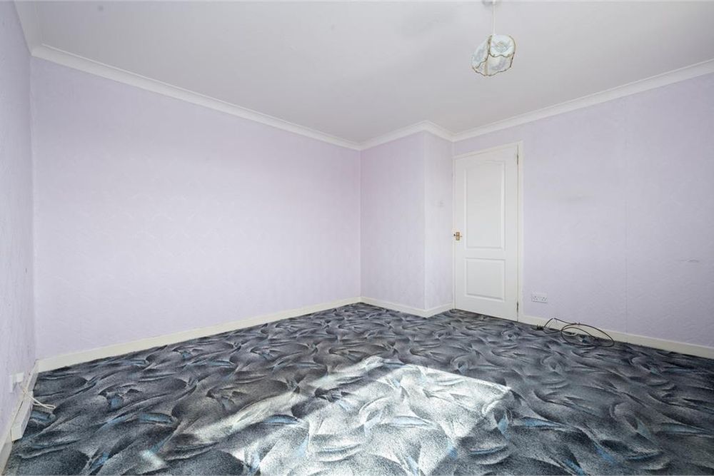 Estate agent photo of an empty room. The walls and ceiling are painted pale lilac. The carpet is an abstract mid-century pattern of greys and blues, a different version of the carpet in the first photo, like coloured oil floating on water.