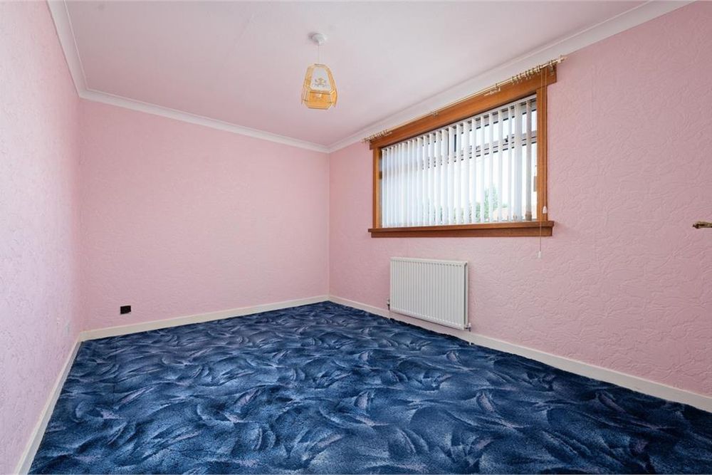 Estate agent photo of an empty room. The walls and ceiling are painted pink. The carpet is an abstract mid-century pattern of blues, like coloured oil floating on water.
