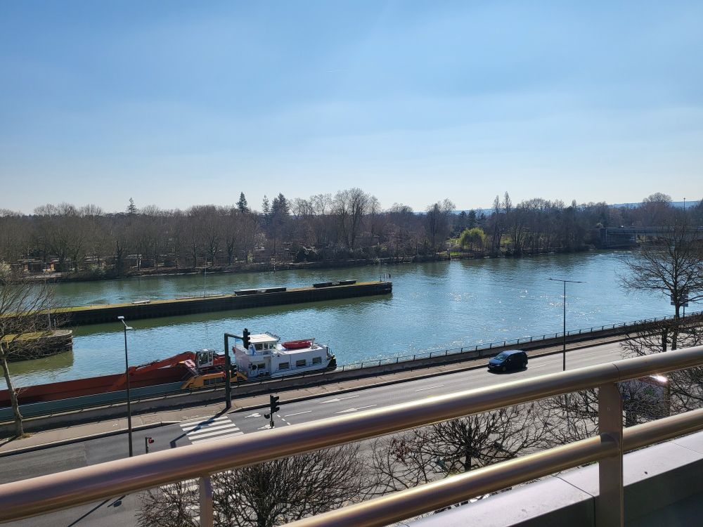 Photo of a view from a terrace high up. The Seine river is clearly visible, and a forest behind it.