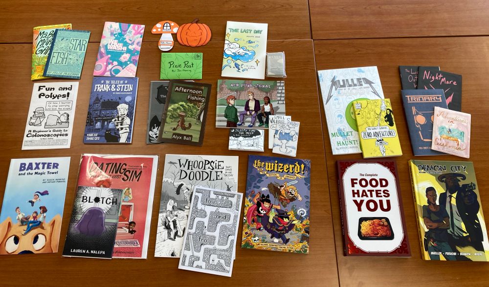 A bunch of comic books, mini comics, etc. arrayed on a faux wood grain tabletop