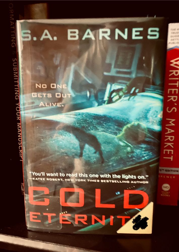 Book COLD ETERNITY by SA Barnes standing face out upright on a black bookshelf.