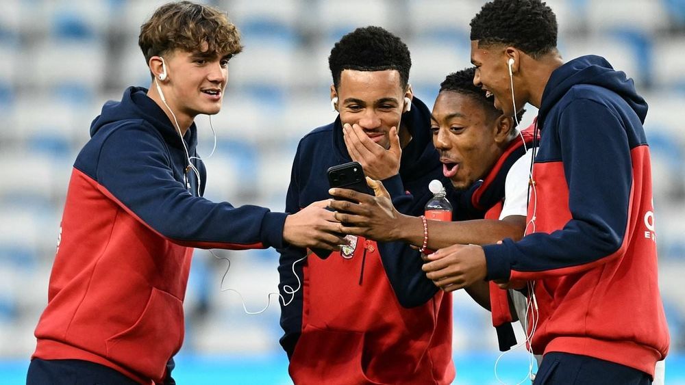 Arsenal youngsters Max Dowman, Ethan Nwaneri, Myles Lewis-Skelly & Andre Harriman-Annous looking at a phone and laughing