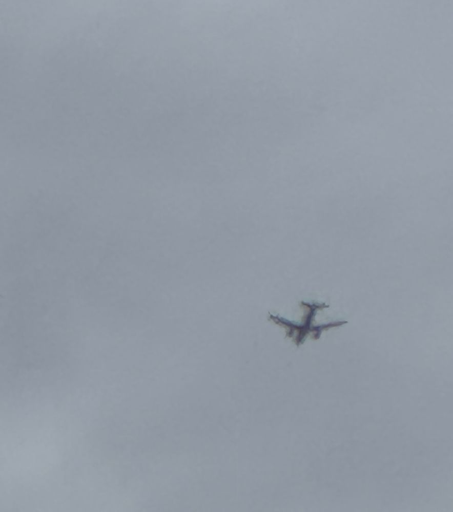 A very very blurry plane shaped shadow flying in amongst heavy grey clouds.