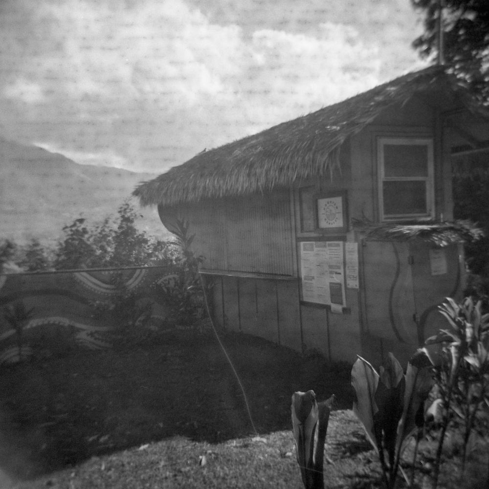 A black and white film photograph of a juice and coffee hut named Nourish Hanalei in Kauai. It stits on a cliff overlooking the Hanalei River. 