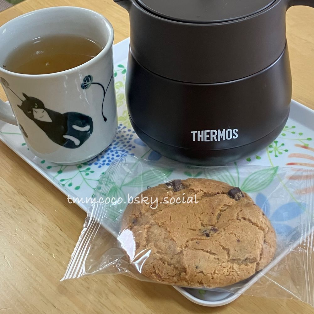 自家製ほうじ茶とタカキベーカリーのチョコチップクッキーを並べてお茶を飲んでいるところ。
白いボタニカル柄のトレーにてのひらサイズのでっかいクッキー、サーモスの保温ティーポット、砥部焼のぽってりした白いマグカップ(味のあるねこちゃんの絵付け)が並んでいる。