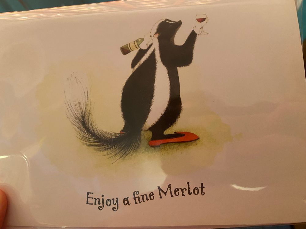 A skunk holding a glass with text that says, “Enjoy a fine Merlot.”