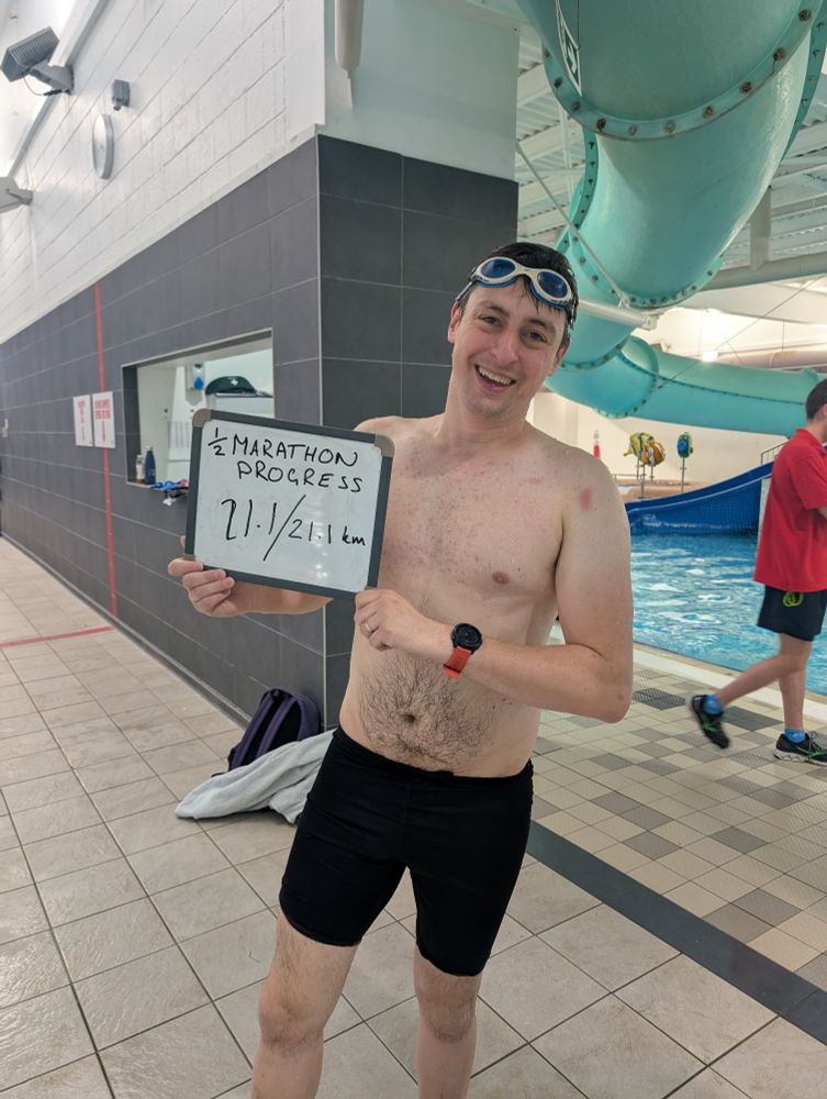 A very tired Simon holds a sign indicating that he has finished his half marathon swim 
