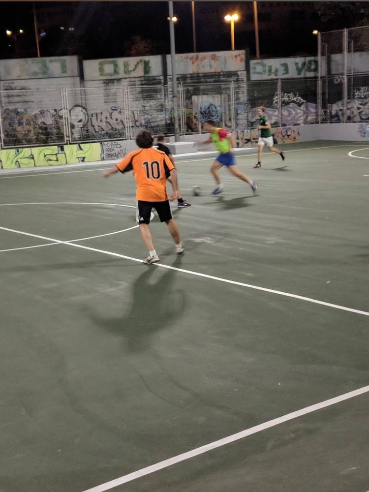 Cancha de fútbol sala bien asfaltada, líneas perfectamente pintadas, con cuatro hombres jugando en ella.